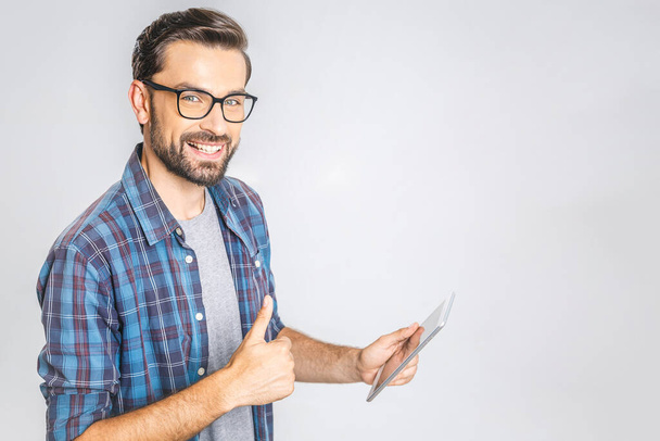 Happy young man in plaid shirt standing and using tablet over grey background. Sign super.  - Photo, Image
