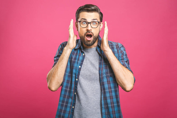 OMG! Ongelofelijk. Portret van een knappe jongeman met een bril die naar de camera kijkt terwijl hij tegen een roze achtergrond staat. close up portret van bebaarde man houden zijn mond open. - Foto, afbeelding