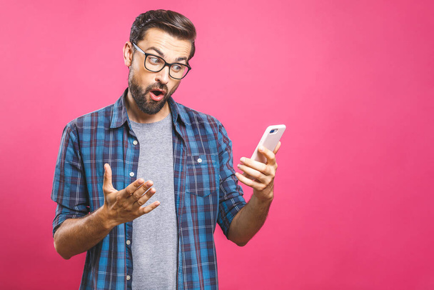 Portrait of a surprised casual man looking at mobile phone isolated over pink background. - Foto, immagini