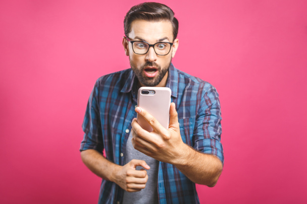Retrato de um homem casual surpreso olhando para o telefone celular isolado sobre fundo rosa
. - Foto, Imagem