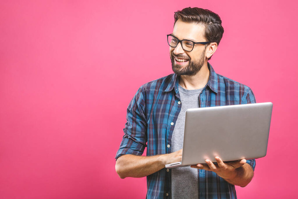 Experto en negocios seguro. Joven hombre guapo de confianza en camisa sosteniendo el ordenador portátil y sonriendo mientras está de pie sobre el fondo rosa
  - Foto, Imagen