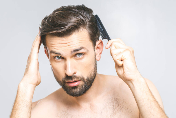 Portrait of handsome young man combing his hair in bathroom. Isolated over grey background.  - Valokuva, kuva