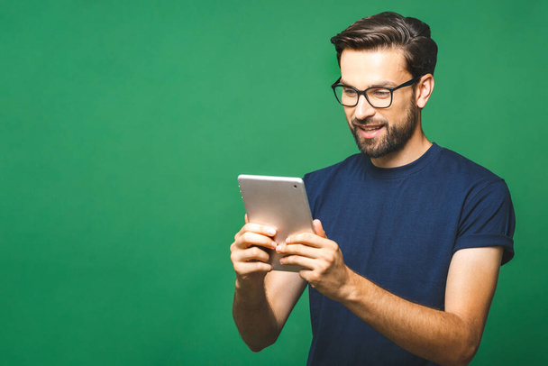 Jeune homme heureux en chemise décontractée et lunettes debout et en utilisant une tablette sur fond vert
 - Photo, image