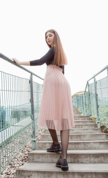 Gyönyörű lány fekete blúzban és rózsaszín szoknyában felmászik a lépcsőn. Fiatal, csinos nő sétál fel a lépcsőn a városban. Vegyél! Varsó. - Fotó, kép