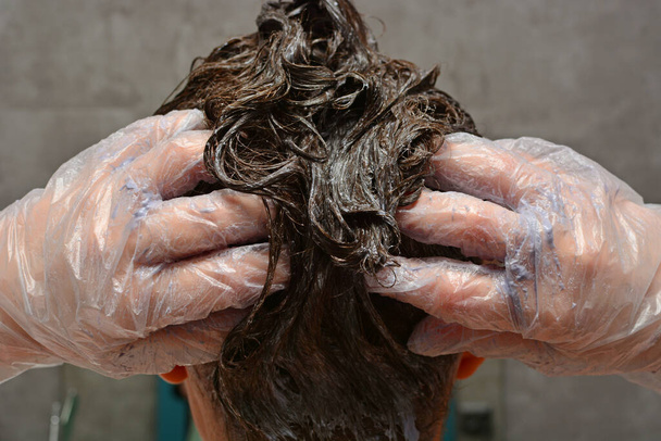 若い女性は家で髪を染めている。女の子は自分の浴室で髪を着色します。検疫、ホームヘアケア、家庭の概念にとどまる. - 写真・画像