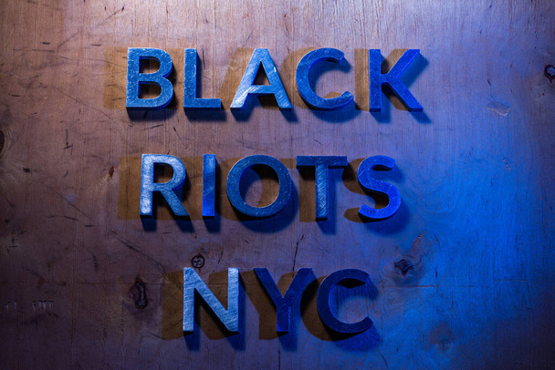 Las palabras disturbios negros NYC colocó con letras de metal en la superficie plana de madera contrachapada bajo luces de la policía blanca y azul. Concepto
. - Foto, imagen