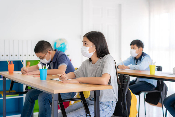 Groupe d'élèves asiatiques du primaire portant un masque hygiénique pour prévenir l'éclosion de Covid 19 en classe pendant la réouverture de leur école, Nouveau concept normal pour l'éducation - Photo, image
