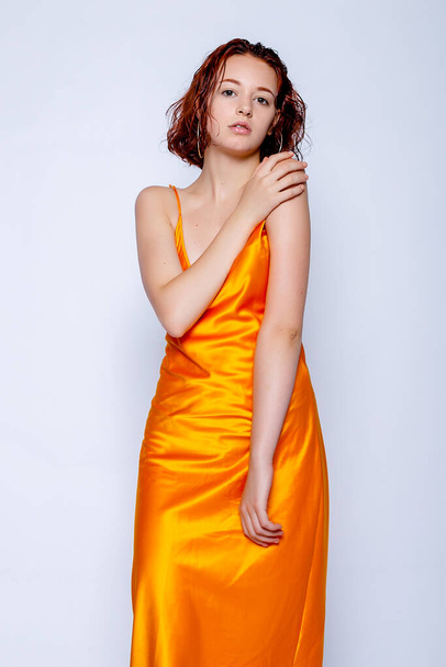 Portrait of attractive girl in orange dress in the studio. Fascinating red-haired lady - Zdjęcie, obraz