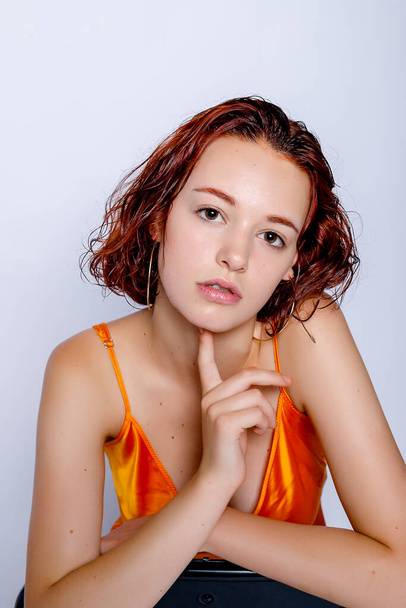 Portrait of attractive girl in orange dress in the studio. Fascinating red-haired lady. closeup portrait sitting on a chair - Valokuva, kuva