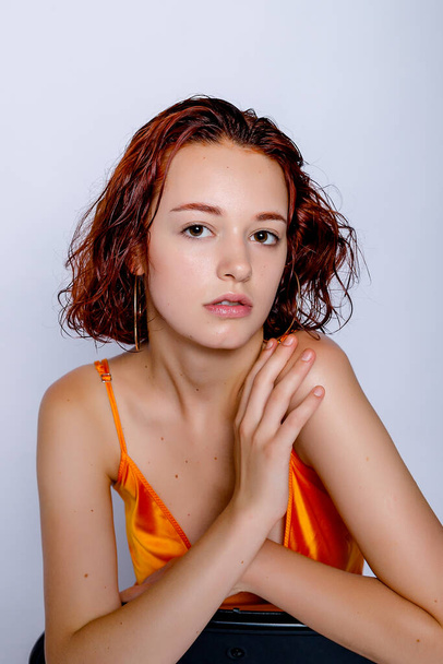 Portrait of attractive girl in orange dress in the studio. Fascinating red-haired lady. closeup portrait sitting on a chair - Photo, Image