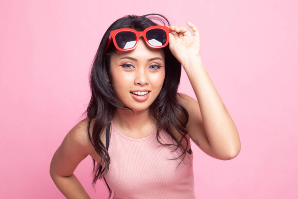 Portrait of a beautiful young asian girl in sunglasses on pink background - Фото, изображение