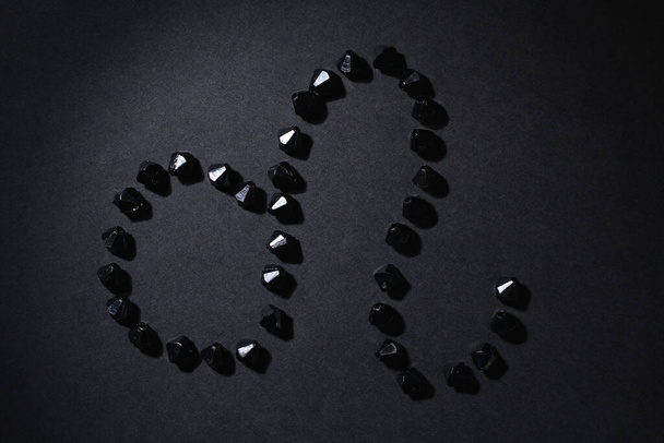 Símbolo do signo zodiacal Leo feito por pedras pretas em um fundo preto. Chave escura baixa. Iluminação de vinheta. Horóscopo tema
 - Foto, Imagem