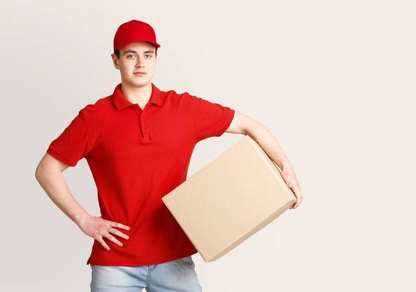 Entrega a domicilio moderna. Mensajero en uniforme rojo sostiene el paquete debajo de su brazo y espera al cliente
 - Foto, imagen