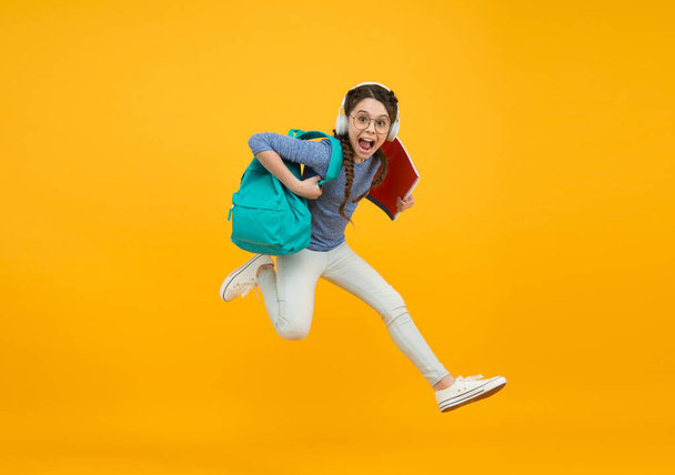 Run skipping along. Energetic girl run to school yellow background. Happy child back to school. Childhood activity. Education and development. Active lifestyle. Run to your future - 写真・画像