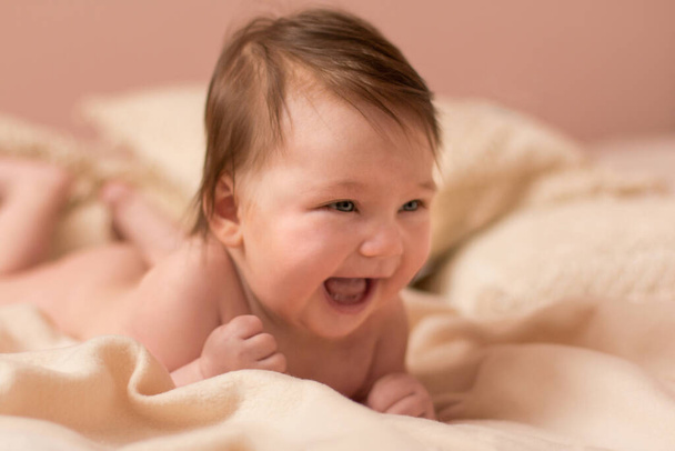 Πορτρέτο αξιολάτρευτο χαμογελαστό νεογέννητο μωρό με πυκνά καστανά μαλλιά. Γυμνό νεογέννητο παιδί χαλαρώνει στο κρεβάτι. - Φωτογραφία, εικόνα