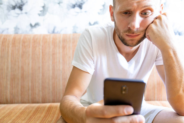 un jeune homme au visage ennuyeux regarde dans l'écran d'un smartphone
 - Photo, image