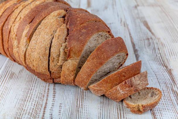 Braunes Brot. Braunes frisches Brot mit Samen wird auf altem Holzgrund in Stücke geschnitten. Kopieren, leerer Raum für Text. - Foto, Bild