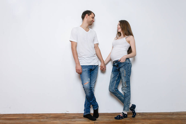 Young married couple embraces standing near the white wall. show a snapshot of an ultrasound. Husband holds pregnant wife's hand. A loving couple, future parents. Lifestyle, happy people. - Photo, image