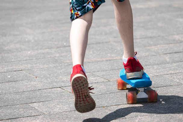 legs of a skateboarder in red sneakers on a blue penny board. pick up speed on a skateboard. teens ride in the park - Foto, Bild