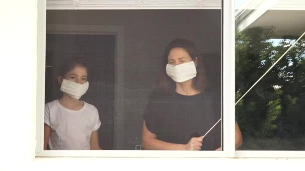 Matka a dcera (10 let) v samovazbě s maskou lékařské tváře při pohledu ven z okna domu s nápisem: Jsme v pořádku s příbuznými. - Záběry, video