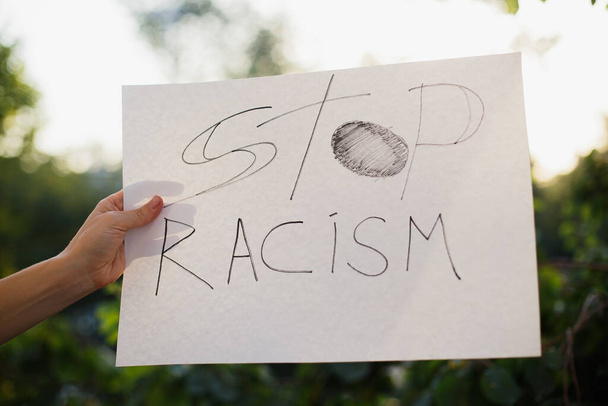 Γυναίκα κρατώντας λευκή βίβλο με κείμενο "Σταματήστε τον ρατσισμό". Με φόντο τα δέντρα και το φως του ήλιου - Φωτογραφία, εικόνα