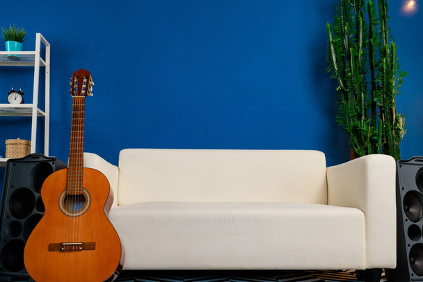 Wooden acoustic guitar near white sofa in modern living room - Фото, изображение