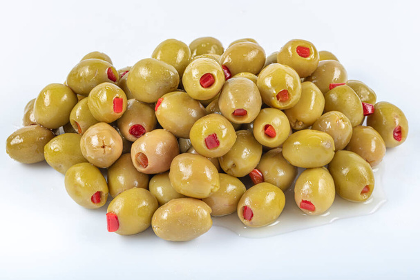 Зеленые оливки, наполненные красным перцем. Зеленые оливки фаршированные красным перцем стоять на белом фоне. Delicatessen - концепция завтрака
. - Фото, изображение