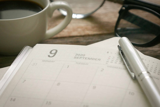 Selectieve focus maandelijkse planner in pagina September samen met een kopje koffie, vergrootglas, pen en bril. September vertegenwoordigen Q3 of kwartaal drie in het bedrijfsleven. - Foto, afbeelding