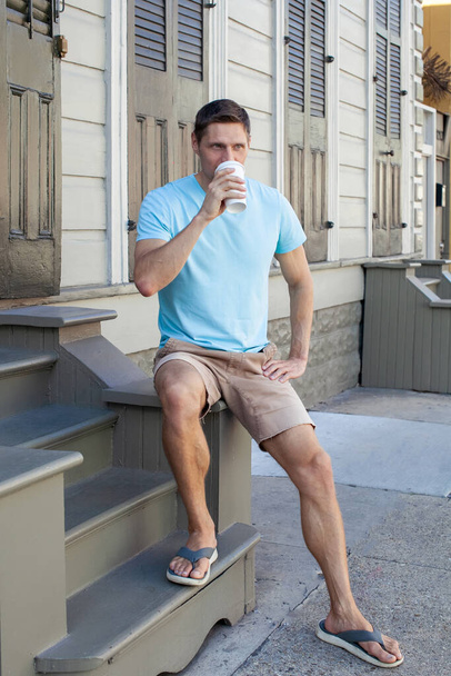 Komea parrakas mies kahvitauolla ulkona. Mies lepää kuistilla ja juo aamukahviaan odottaessaan ystäviä.. - Valokuva, kuva