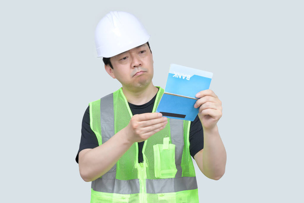 Egy középkorú ázsiai mérnök, kezében egy bankkártyával, szürke alapon.. - Fotó, kép
