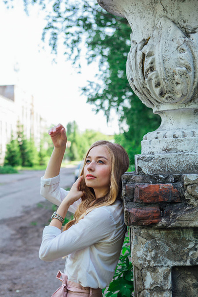 Portrait of a beautiful blond girl standing next to an old building with a decorative antique vase and stairs - Foto, afbeelding