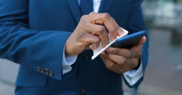Close up of smartphone in hands of African American businessman in suit and tie. Man cleaning phone with disinfecting napkin. Cellphone disinfection outdoor. - Séquence, vidéo