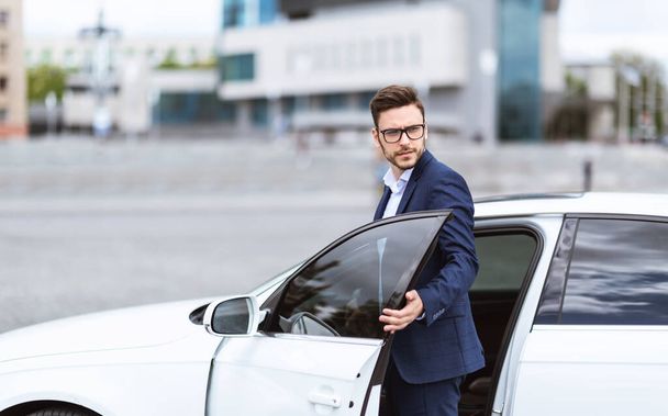 ダウンタウンエリア、コピースペースで彼の車に乗るスタイリッシュなスーツで魅力的な白人起業家 - 写真・画像