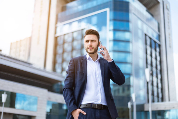 Executivo de negócios atraente falando no celular em frente ao prédio de vários andares
 - Foto, Imagem