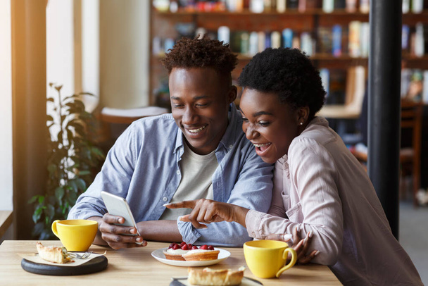 Ρομαντικές στιγμές. Όμορφο ζευγάρι από την Αφρική Αμερικής με smartphone σε ημερομηνία στην καφετέρια - Φωτογραφία, εικόνα
