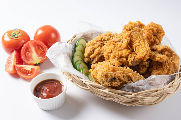 Crispy fried chicken on wicker basket  serve with cucumber and  ketchup on white background. - Photo, Image
