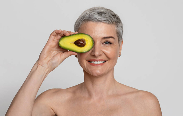Natural Skincare. Naked Beautiful Mature Woman Covering Eve With Avocado Half - Φωτογραφία, εικόνα