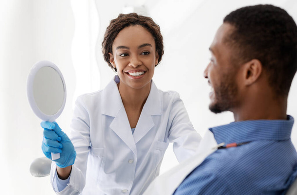 Dentista mostrando espejo paciente para comprobar su nueva sonrisa
 - Foto, Imagen