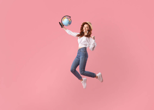 Happy Traveler Girl Jumping Holding Globe Gesturing Igen, rózsaszín háttér - Fotó, kép