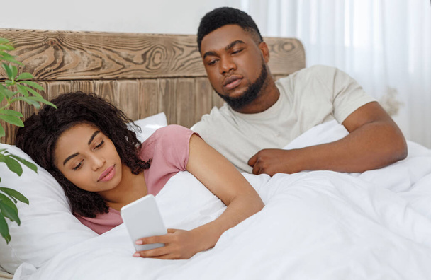 zwart meisje chatten met minnaar op mobiele telefoon in bed - Foto, afbeelding