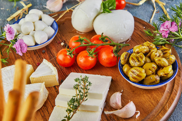 Mozzarella babybrie kaas, Bulgaarse kaas en mozzarella Fresca met knoflook en druiven en een glas wijn op een houten statief op een blauwe achtergrond. Italiaanse lekkernijen. - Foto, afbeelding