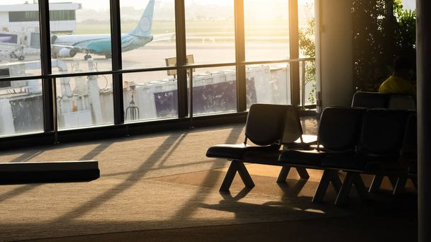 Vista de silueta de sillas en el aeropuerto terminal por la mañana con la salida del sol y el avión en el fondo
.  - Foto, Imagen