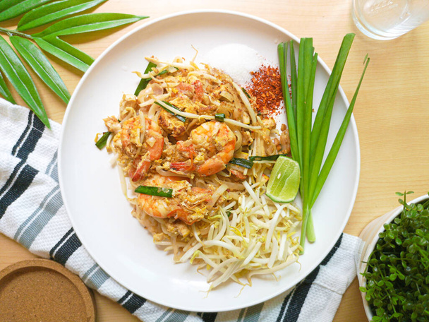Vista superior da Tailândia estilo tradicional macarrão comida, macarrão de arroz frito com chamada de camarão Pad Thai Goong Sod em prato branco com pimenta açúcar amendoim e limão para tempero em mesa de madeira
. - Foto, Imagem