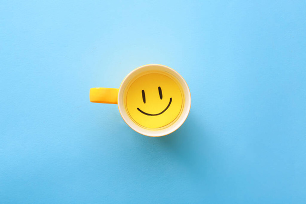 Cup with paper smile on color background - Photo, Image