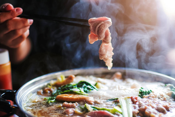 Woman holding sliced beef meat by chopsticks shabu shabu is Korean or Japanese style beef in hot pot dish of thinly sliced meat and vegetables boiled in water. delicious food most popular in thailand. - Fotografie, Obrázek
