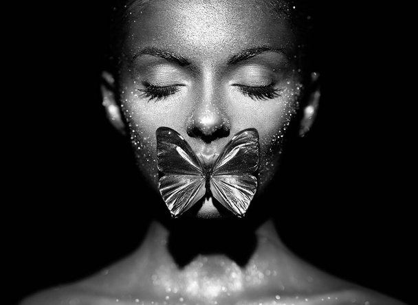 Fashion model woman in bright sparkles and lights posing in studio. Portrait of beautiful sexy woman with butterfly. Art design glitter glowing make up. Black and white photography - Фото, зображення