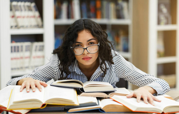 Estudante cansado apoiando-se em livros na biblioteca do campus
 - Foto, Imagem
