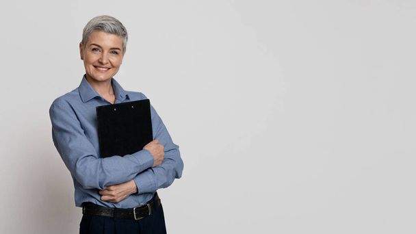 Portrét úspěšné dospělé podnikatelky se schránkou v rukou na světlém pozadí - Fotografie, Obrázek
