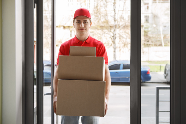 Online tilaus ja moderni postipalvelu. Kuriiri punaisessa univormussa omistaa monia laatikoita - Valokuva, kuva