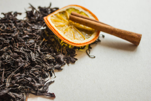 Selected leaves of fermented tea, a traditional drink. In the distance, orange and cinnamon, the background is blurred. Tea with aromatic additives, spices. - Photo, Image